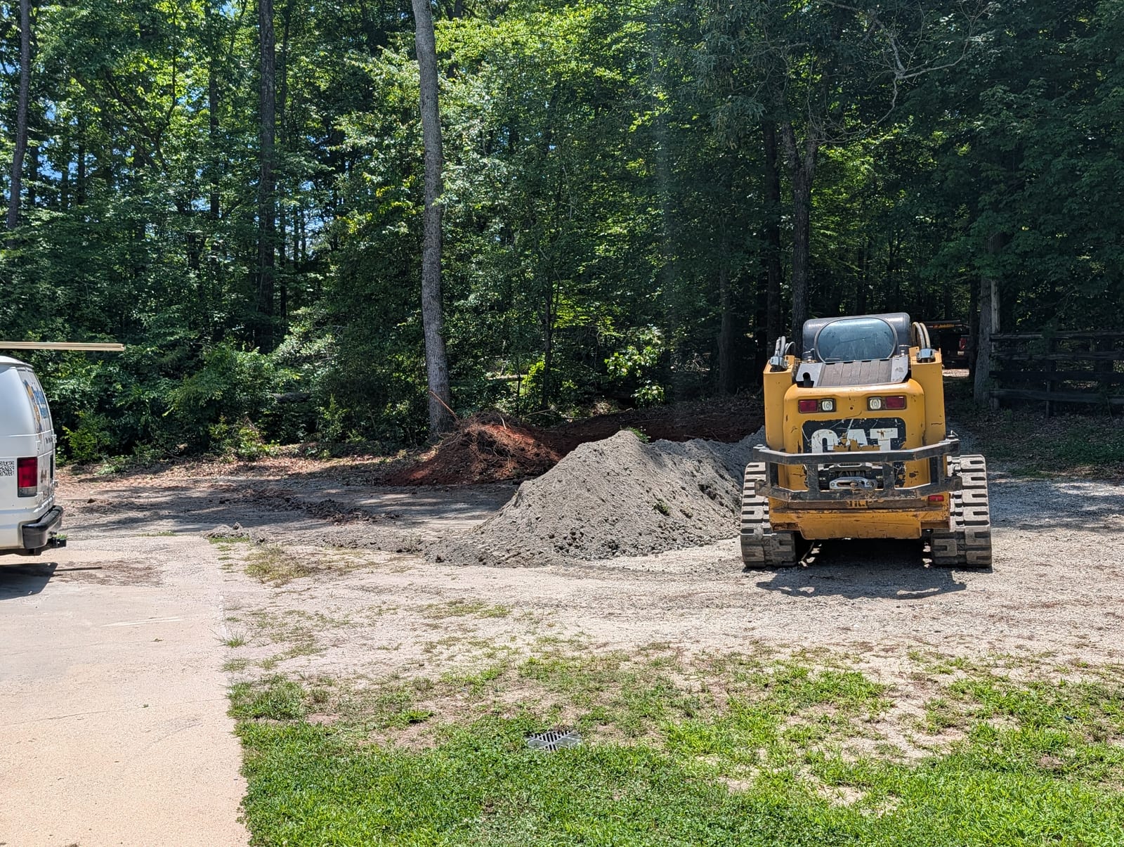 Skid steer at the house end of the driveway during the regrade, with stone and spoil piles